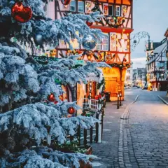 Verschneiter Weihnachtsbaum mit roten Kugeln vor Fachwerkhäusern, die mit Lichtern geschmückt sind. Perfekte reiseziele winter.
