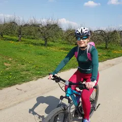 Kobieta na rowerze podziwia sandomierskie trasy rowerowe wśród kwitnących sadów.