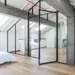 Moderno recupero sottotetto con pareti in vetro, travi a vista in cemento e parquet chiaro. Ambiente luminoso con cucina e zona living.