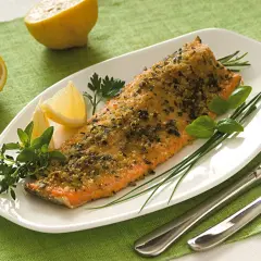 Deliziosa trota salmonata al forno, croccante e profumata, servita con limone e erbe aromatiche fresche.