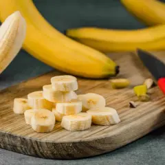 Plasterki banana na desce, idealne na pusty żołądek. Obok leży nóż z czerwoną rączką.