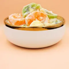 Pyszna sałatka owocowa z pomarańczy, kiwi i ananasa w kremowym sosie, podana w eleganckiej miseczce ze złotym rantem.