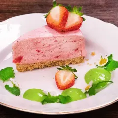 En bit krämig cheesecake jordgubb med färska bär och mynta på en vit tallrik.