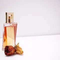 Elegancka butelka perfum z płynem w kolorze bursztynu i dwoma zasuszonymi różami. Czy tak pachnie piżmo?