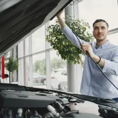 Un homme examine le moteur d'une voiture neuve dans un showroom. Il s'assure de la qualité avant de finaliser le prix de l'expertise voiture.