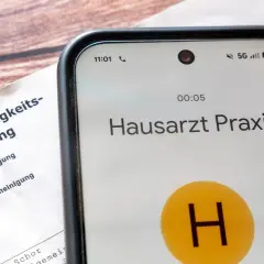 Arbeitsunfähigkeitsbescheinigung liegt bereit. Das Handy zeigt Anruf bei Hausarzt Praxis. Wichtig für Krankmeldung ab 3. Tag Gesetz.