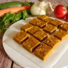 Cubetti di dado vegetale fatto in casa, pronti per insaporire ogni piatto. Verdure fresche come carote, zucchine e pomodori sullo sfondo.
