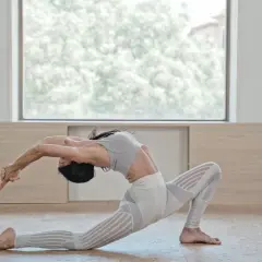 Mujer en postura de Anjaneyasana yoga, arqueando la espalda y extendiendo brazos hacia atrás.