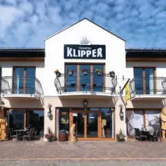 Tawerna "Klipper" we Władysławowie z drewnianymi rzeźbami i stolikami na zewnątrz.