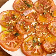 Carpaccio de tomate fresco con aceite de oliva, ajo picado y hierbas aromáticas. Un plato ligero y lleno de sabor.