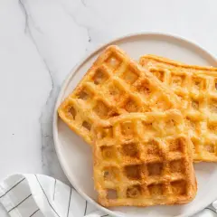 Trois gaufres au sarrasin dorées et croustillantes sur une assiette blanche, prêtes à être dégustées.