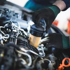 Mechanik w czarnych rękawiczkach dokonuje wymiany filtra paliwa w silniku samochodowym.