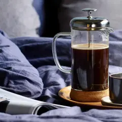 En franskpress med kaffe bredvid en tidning och en kopp. En lugn morgon med kaffe, inte espresso.