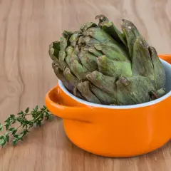 Un gros artichaut vert prêt pour la cuisson Cookeo, avec une branche de thym frais à côté.