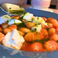 Pyszne makaron gnocchi z pomidorami, mozzarellą i zielonym sosem. Łyżka z sosem czeka na dodanie.