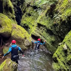 Dwie osoby w kombinezonach i kaskach przemierzają wąski, porośnięty mchem kanion. To właśnie jest canyoning!