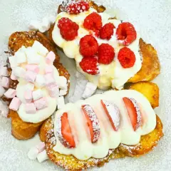 Pyszne tosty francuskie z serem, udekorowane malinami, piankami i truskawkami, posypane cukrem pudrem.