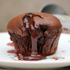Coulant de chocolate tibio con centro líquido, servido en un plato blanco con dibujos de colores.