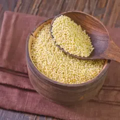 Drewniana miska pełna kaszy jaglanej, która nie zawiera glutenu. Łyżka z kaszą spoczywa na brzegu miski.