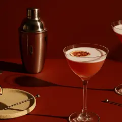 Elegancki drink z brandy, ozdobiony plasterkiem suszonej pomarańczy, obok shakera i figi.