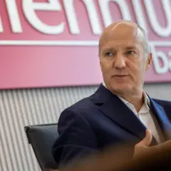 Mężczyzna w garniturze siedzi przed logo Banku Millennium. Kto jest właścicielem banku Millennium?