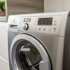 Pralka Electrolux z wyświetlonym błędem E20. Na blacie obok stoją złożone ręczniki i roślina.