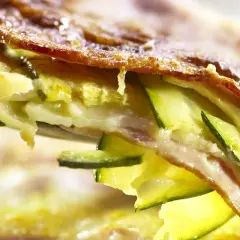 Una fetta di parmigiana di zucchine bianca, con strati di zucchine, formaggio filante e una crosticina dorata.