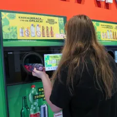 Kobieta wrzuca plastikową butelkę do automatu, który obsługuje system kaucyjny. To ekologiczne rozwiązanie, które zwraca pieniądze.