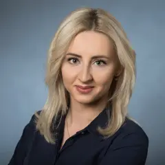 Portret uśmiechniętej blondynki w granatowej koszuli na niebieskim tle.