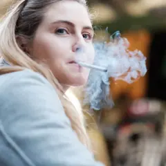 Ragazza bionda con sigaretta tra le labbra, fumo denso che le avvolge il viso. Un momento di pausa, forse dopo essersi lavata i denti, per fumare.