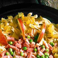 En närbild på en läcker pastasallad med skinka, äppelklyftor och gröna ärtor. En perfekt sommarmåltid!