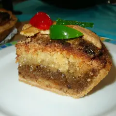 Rebanada de tarta de Mondoñedo, con capas de bizcocho y relleno dulce, decorada con una cereza y un trozo de fruta escarchada verde.