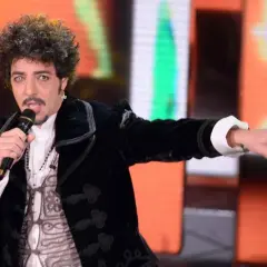 Max Gazzè canta con microfono, vestito elegante, con un'espressione intensa. Sembra che stia raccontando storie con i suoi testi, come se fosse "sotto casa".