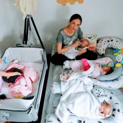 Mama karmi jedno z czworaczków, podczas gdy starsza siostra opiekuje się drugim dzieckiem w łóżeczku.