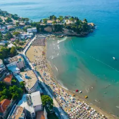 Słoneczne kotor plaże tętnią życiem. Tłumy ludzi odpoczywają pod parasolami, a w turkusowej wodzie kąpie się wielu plażowiczów.