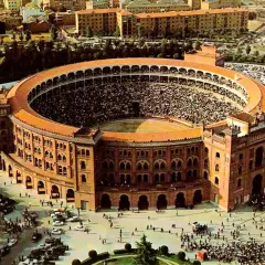 Vista aérea de la plaza de toros Las Ventas, llena de espectadores, con coches aparcados alrededor y gente paseando.