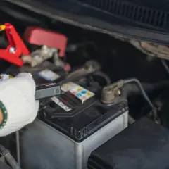 Ręka w białej rękawiczce podłącza prostownik do akumulatora. Wreszcie, kiedy prostownik pokazuje, że akumulator jest naładowany, można ruszać.