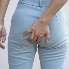 Mano che si gratta il **prurito fondoschiena** attraverso i pantaloni grigi.