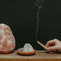Lámpara de sal rosa, cristales y un palo de incienso humeante.