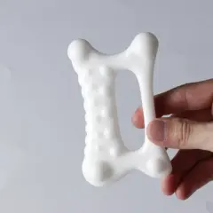 En hand håller ett vitt, benformat verktyg för gua sha massage kropp.