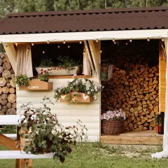Charmante Holzunterstand Ideen: Ein gemütlicher Schuppen mit Blumenkästen, Lichterketten und einem Stapel Brennholz.