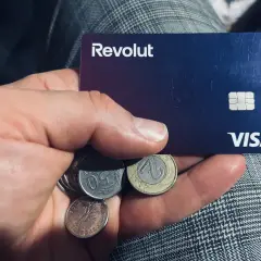 Dłoń trzyma kartę Revolut i polskie monety. Kto jest właścicielem Revolut? To pytanie, na które odpowiedź znajdziesz w aplikacji.