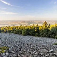 Kamieniste zbocze schodzi ku lasowi, a za nim rozciąga się krajobraz pól i łąk. Widok z łysicy zapiera dech.