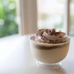 Delicioso mousse de café con crema batida y cacao espolvoreado, servido en un vaso transparente.