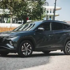 Ciemnoszary Hyundai Tucson 2020 zaparkowany na brukowanej ulicy, z nowoczesnym budynkiem w tle.