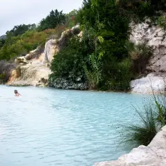 Bagno Vignoni: cascate naturali con acqua azzurra e vegetazione lussureggiante. Due persone nuotano nelle terme.