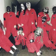 Zespół Slipknot w czerwonych kombinezonach i charakterystycznych maskach, pozuje do zdjęcia w korytarzu.
