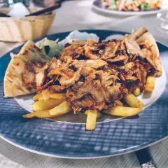 Pyszna szarma z kurczaka z frytkami i pitą na talerzu.