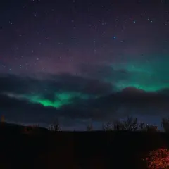 Zielona zorza polarna tańczy na nocnym niebie nad Islandią, wśród gwiazd i ciemnych chmur.