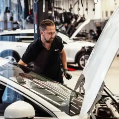 Mekaniker inspekterar en bil med öppen motorhuv. Frågan "hur lång tid tar en bilservice" kan besvaras snabbt med professionell hjälp.
